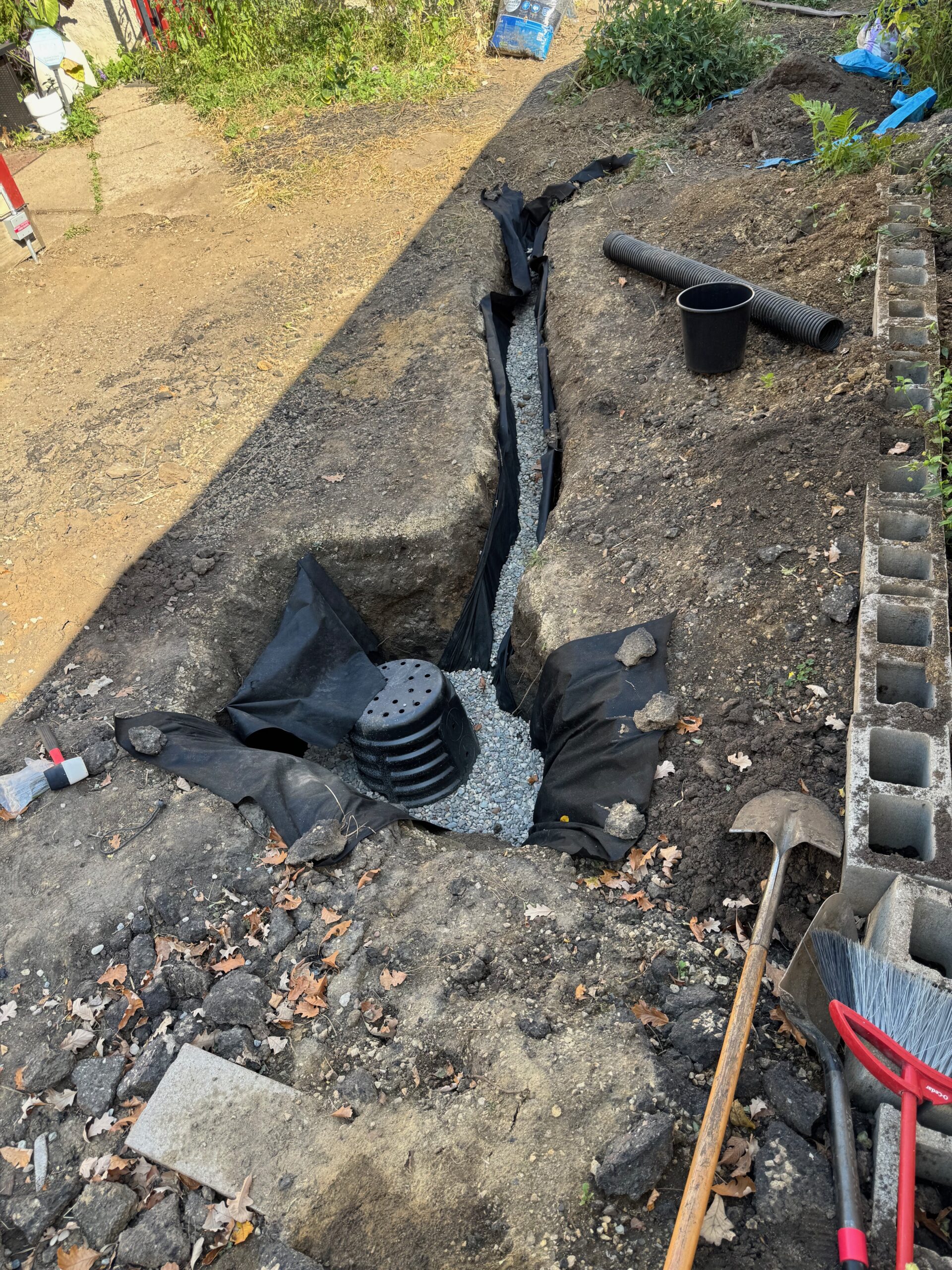 Drainage trench with gravel and a catch basin dug beside the driveway