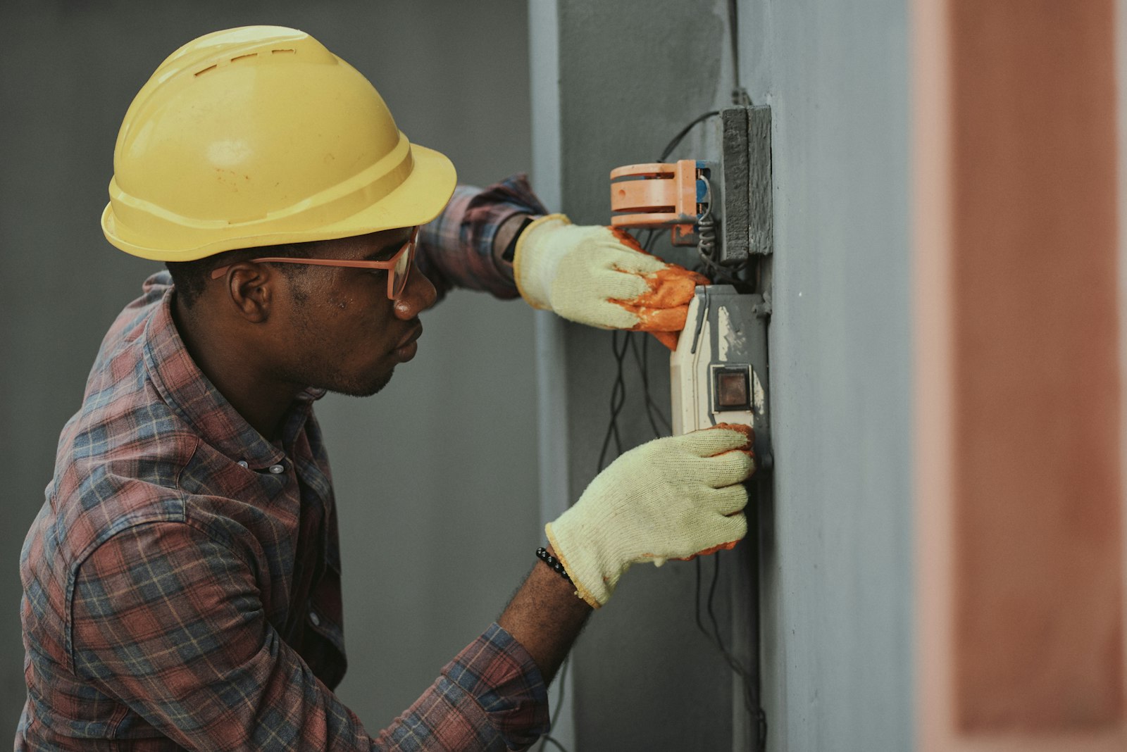 An electrician in a hard hat installing wiring on a job site