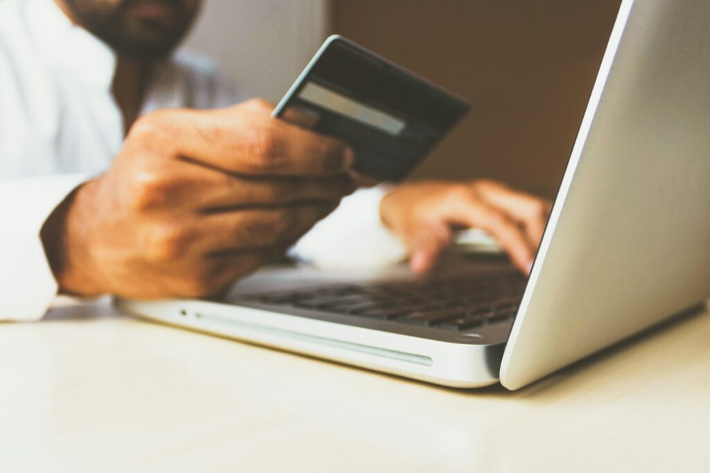 A person at a laptop holding a payment card while reviewing an account on screen