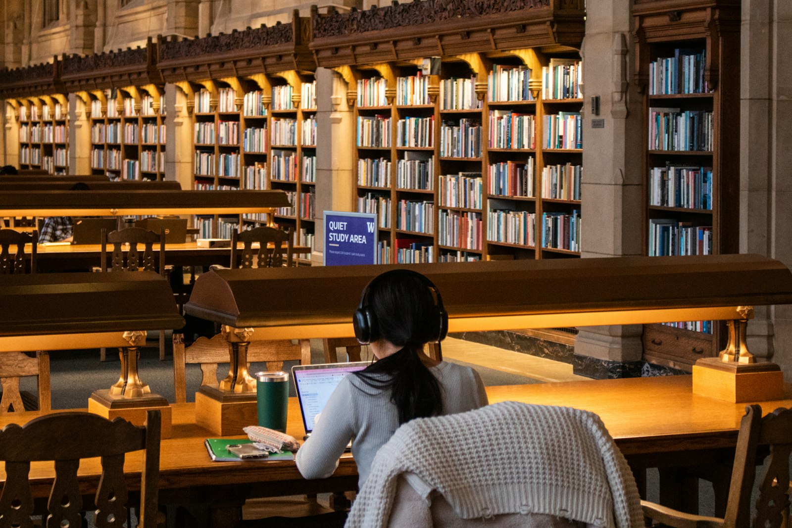 A student working at a library table surrounded by books and notes