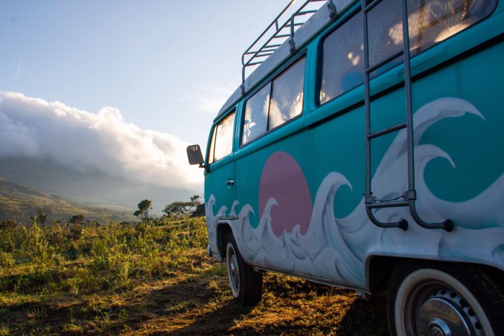 Stock photo of a van with a surfboard painted on the side parked in a grassy field
