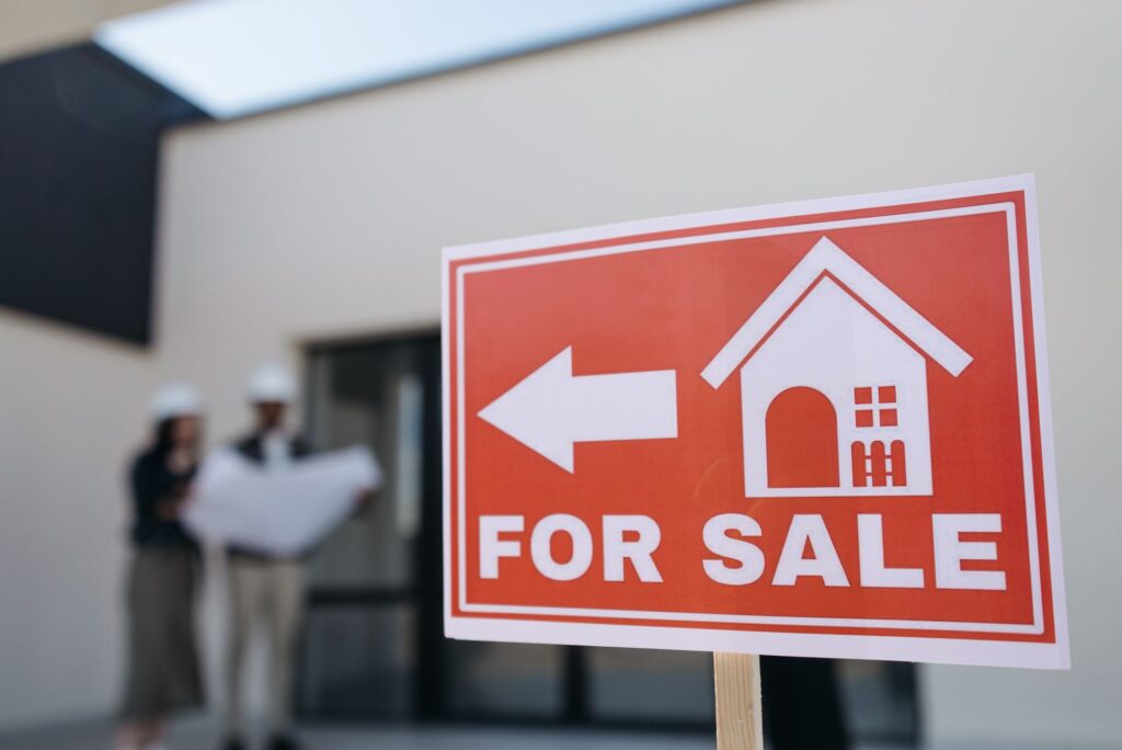 Stock photo of a red For Sale sign in front of a modern house with people behind it
