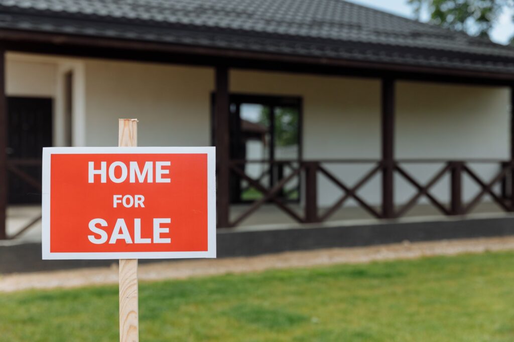 Stock photo of a Home For Sale sign on a lawn in front of a house