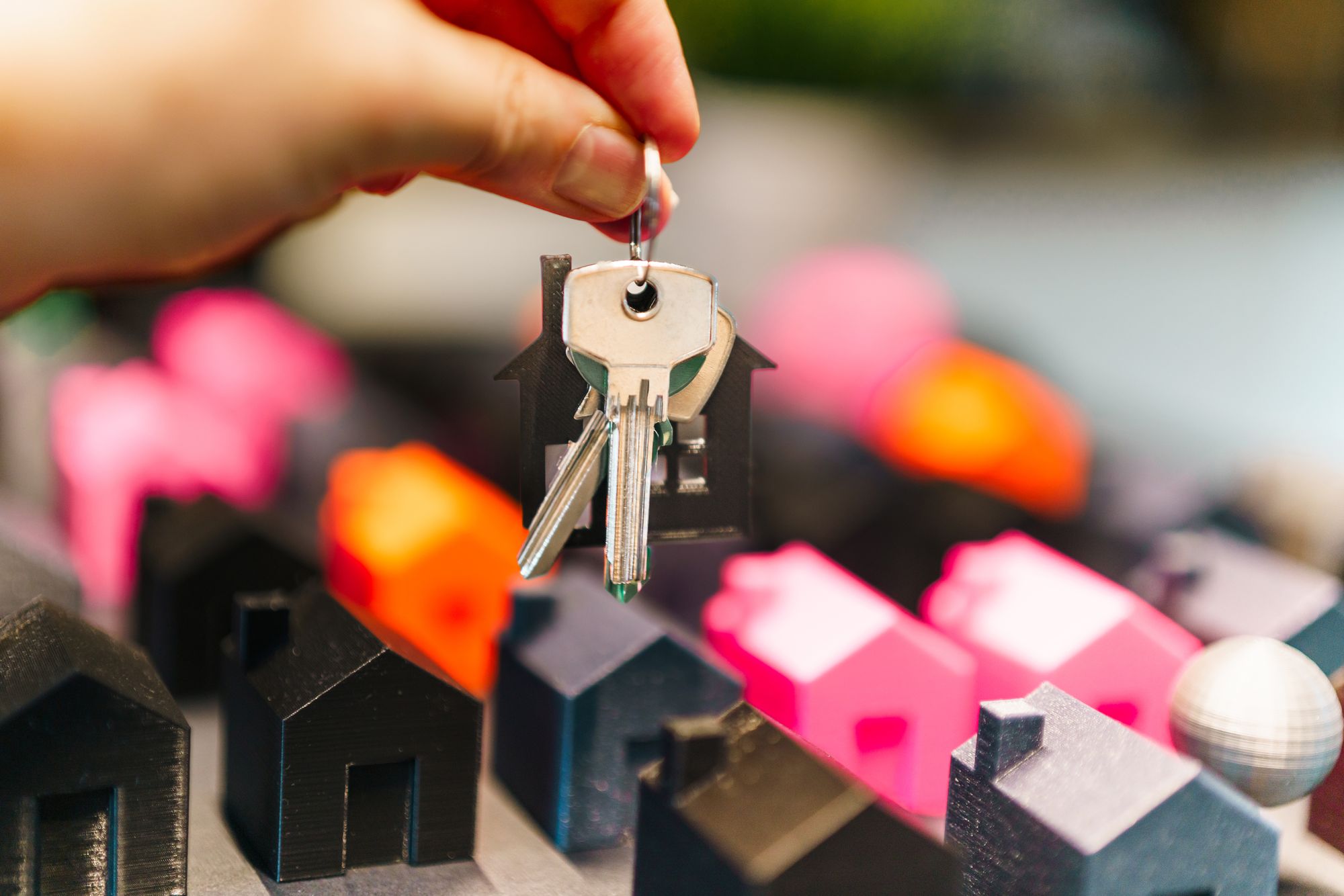 Stock photo of a hand holding house keys above a row of small model houses