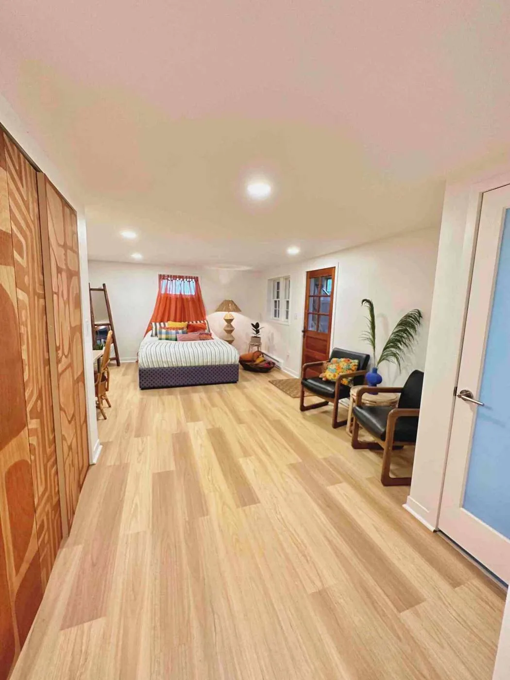 The finished basement suite in my duplex: light wood floors, a bed at the far end, plants by the door