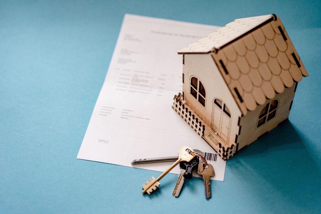 Contract, house keys and a small wooden house model on a table