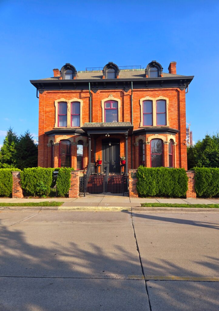 Red brick Victorian house with greenery under a clear blue sky