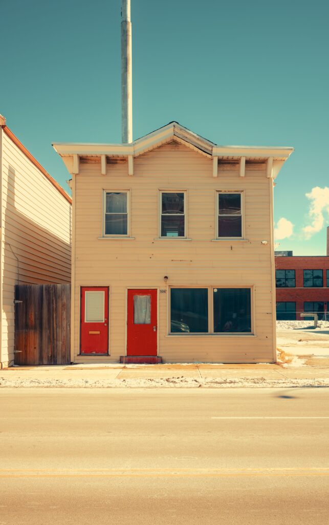 Vintage two-story frame house with two red front doors on a sunny day
