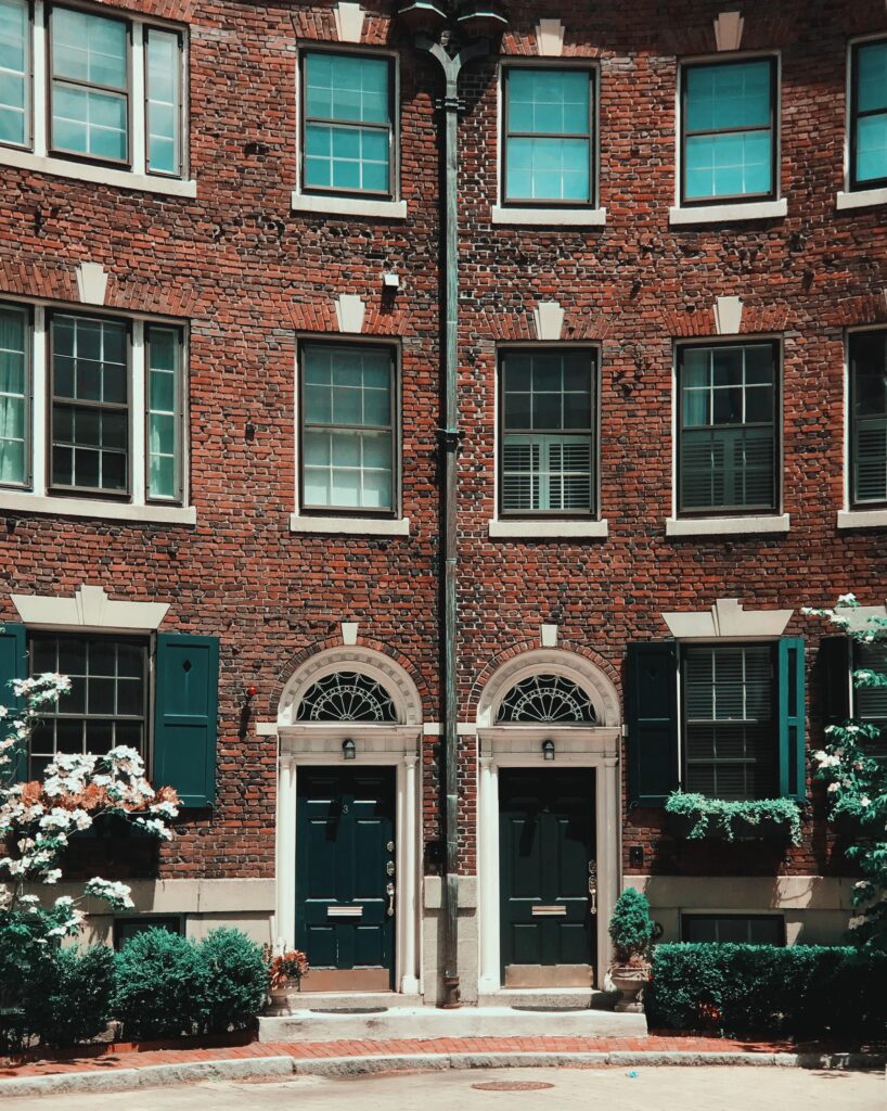 Red brick Boston rowhouse with two arched doorways, green shutters and climbing ivy