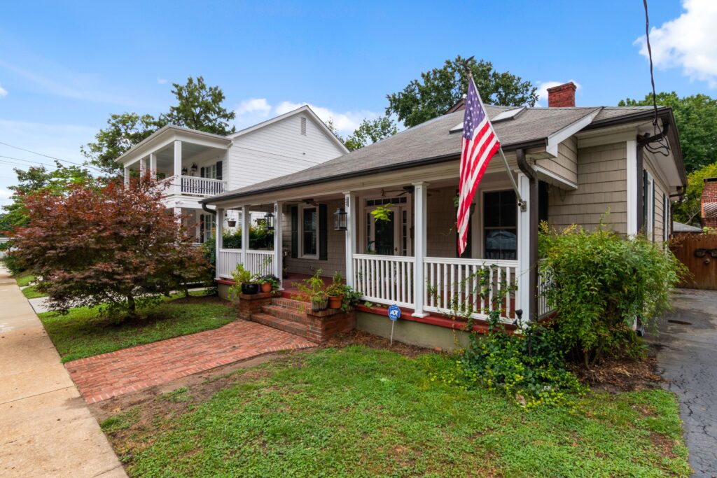Bungalow with a front porch, American flag, brick walkway and garden on a sunny day