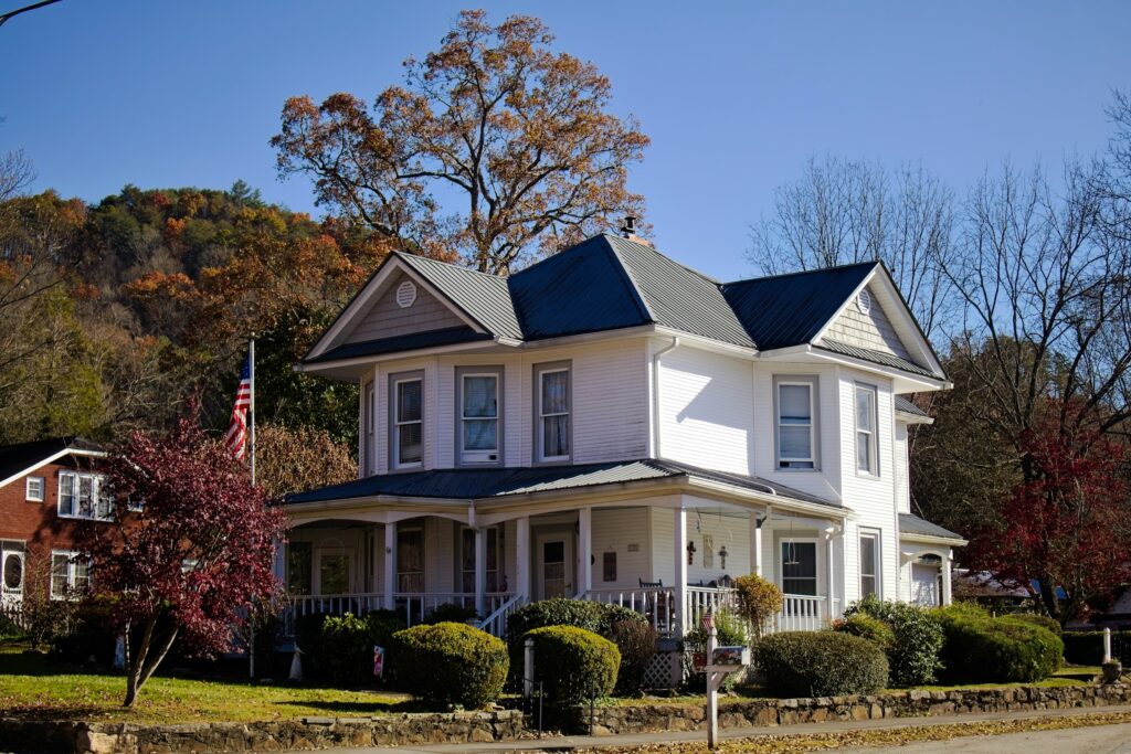 White two-story Victorian house with a wraparound porch and autumn leaves in Andrews, North Carolina