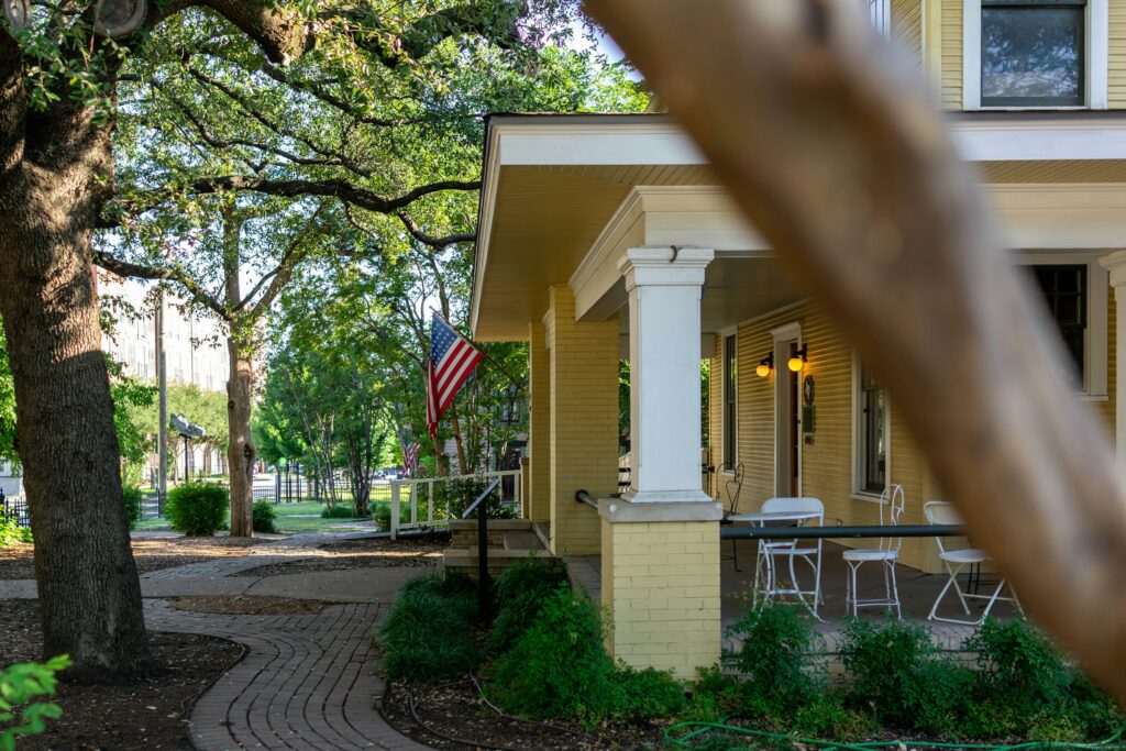 Yellow historic house with a front porch, American flag and brick path in McKinney, Texas