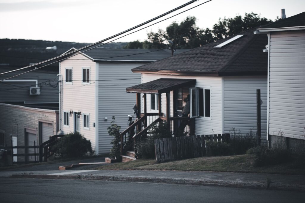 Quiet residential street with modest older houses and a wooden fence at dusk
