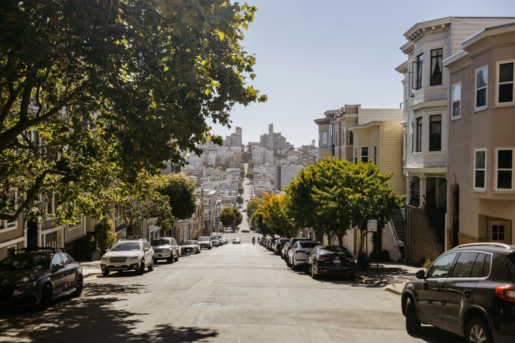 A steep city street lined with older houses and parked cars