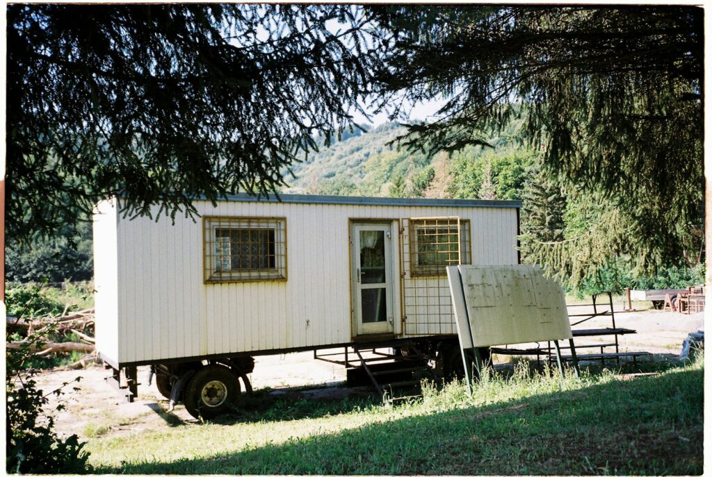 A small white cabin on a wheeled trailer among green trees