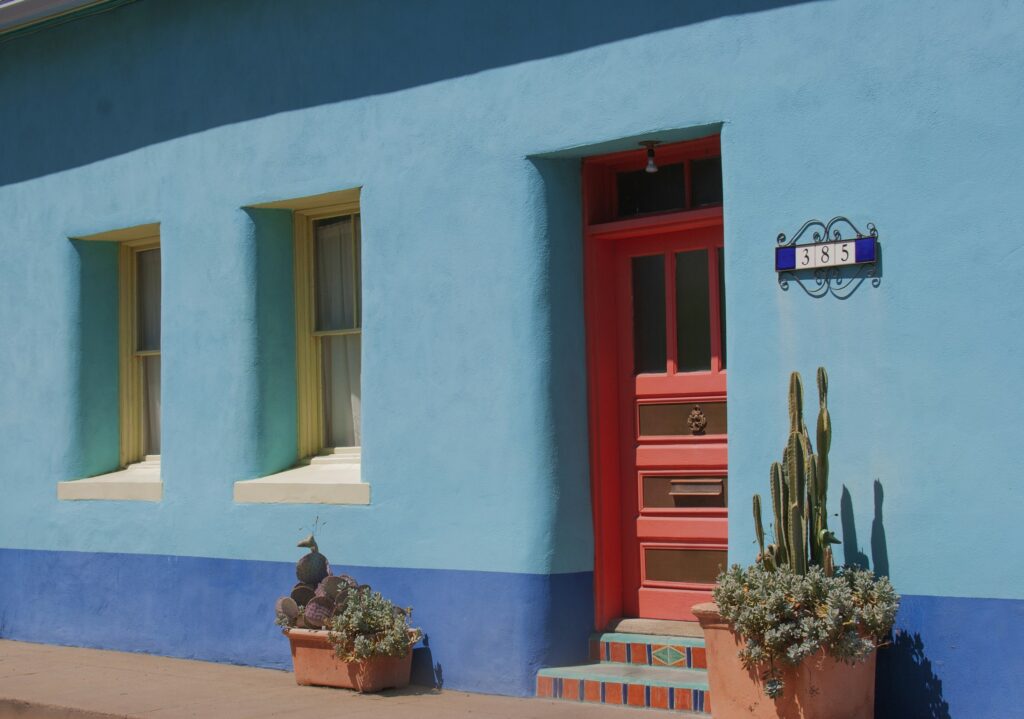 Old blue adobe house with a red door and a cactus in front in Tucson, Arizona