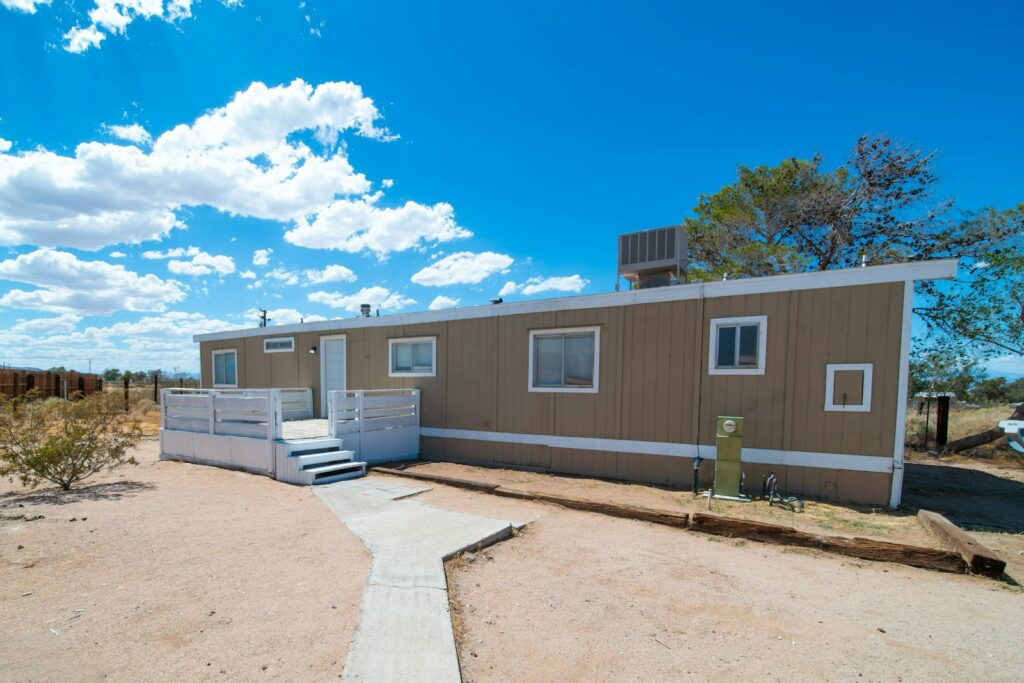 A single-section manufactured home with a wooden deck and steps on a dry lot