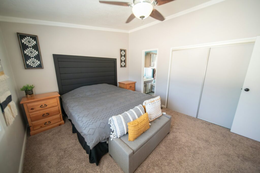 A simple rented room with a made bed, a dresser and daylight from the window
