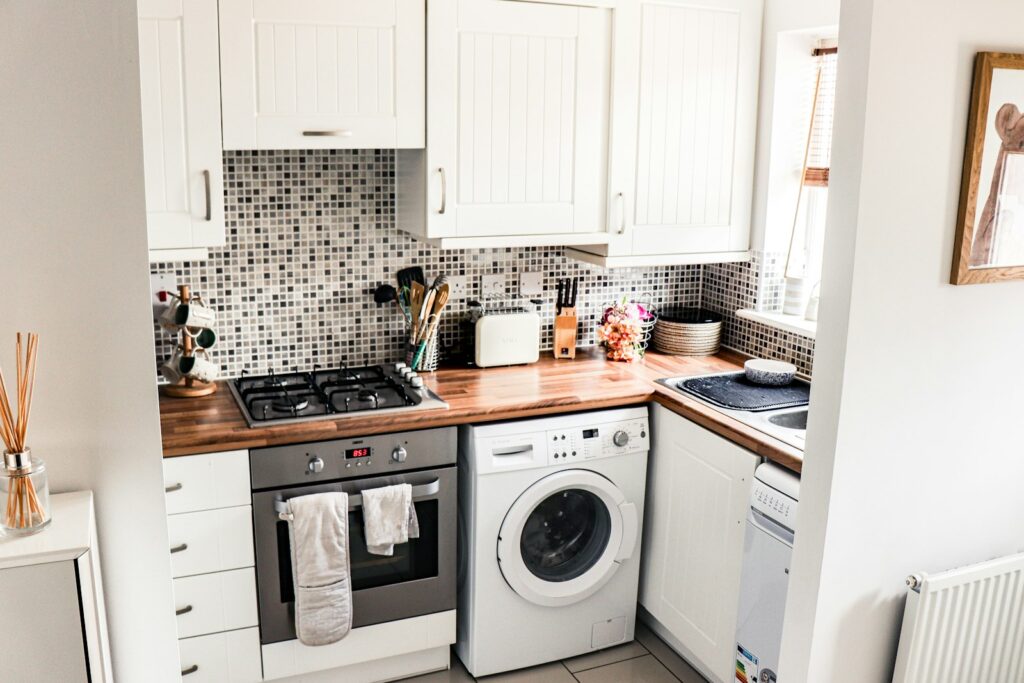 A small kitchen with a stove, a front-load washer and open shelves