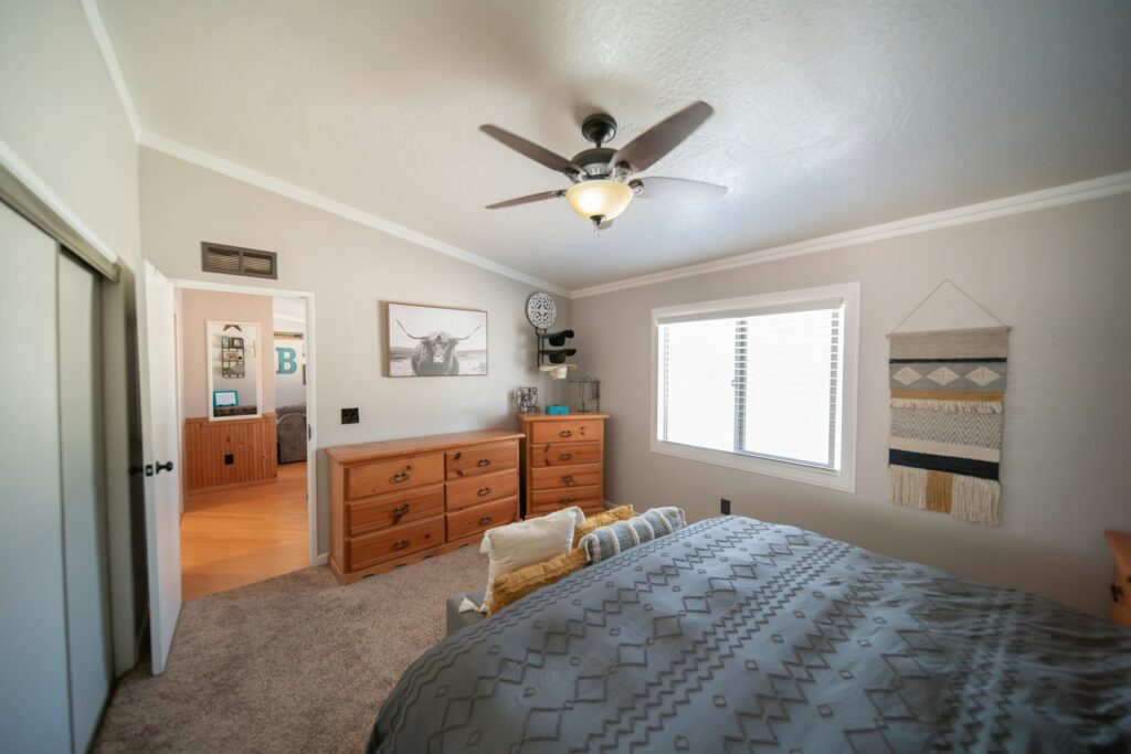 A plain furnished bedroom with a bed, a dresser and a ceiling fan