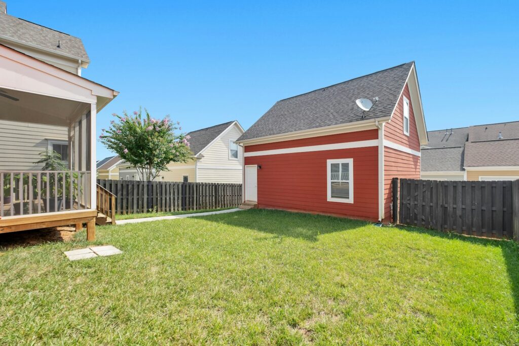 A small red detached building at the back of a fenced lawn, seen from the main house deck